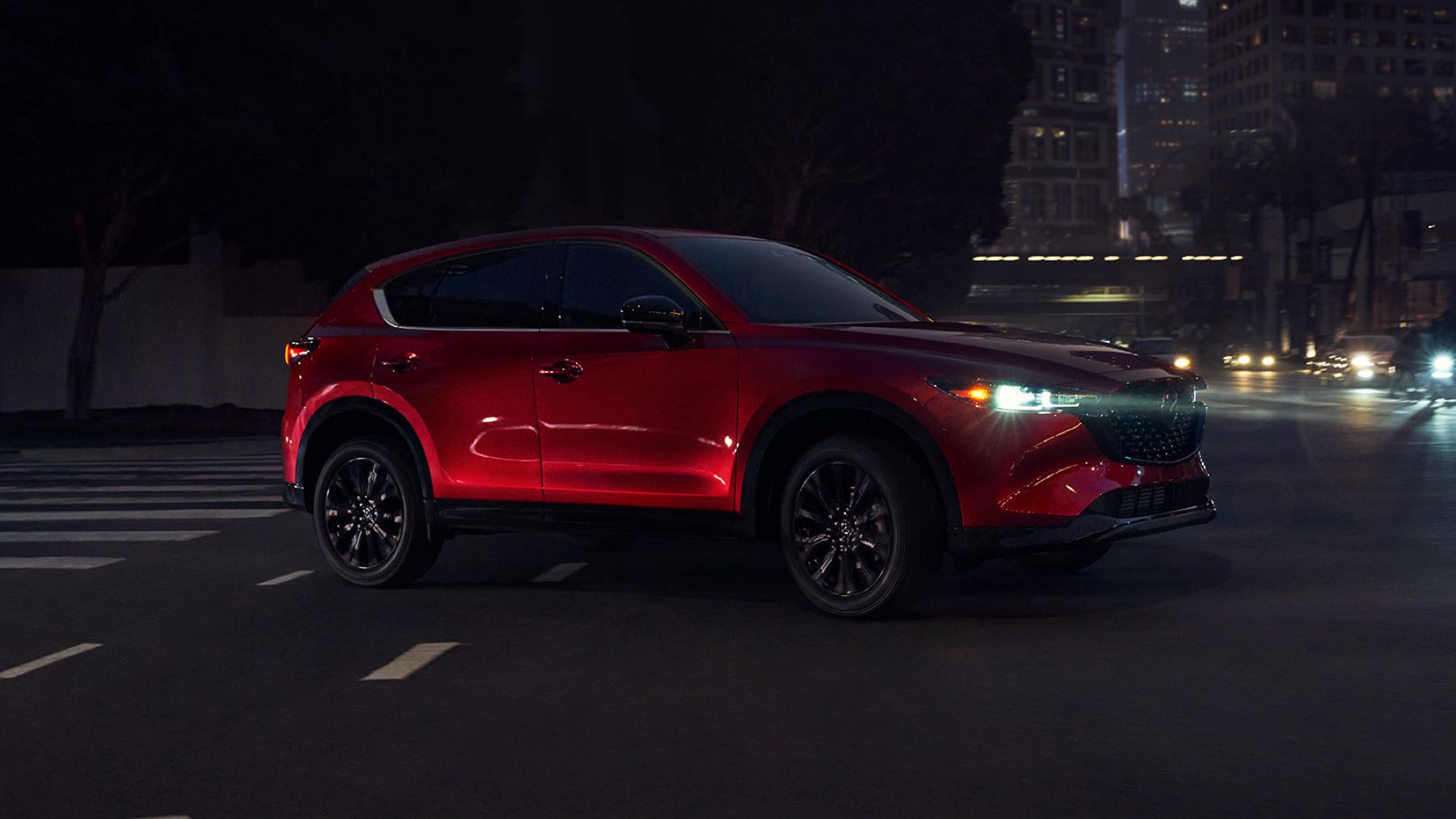 The 2022 Mazda CX-5 compact crossover SUV in red driving at night with its headlights on
