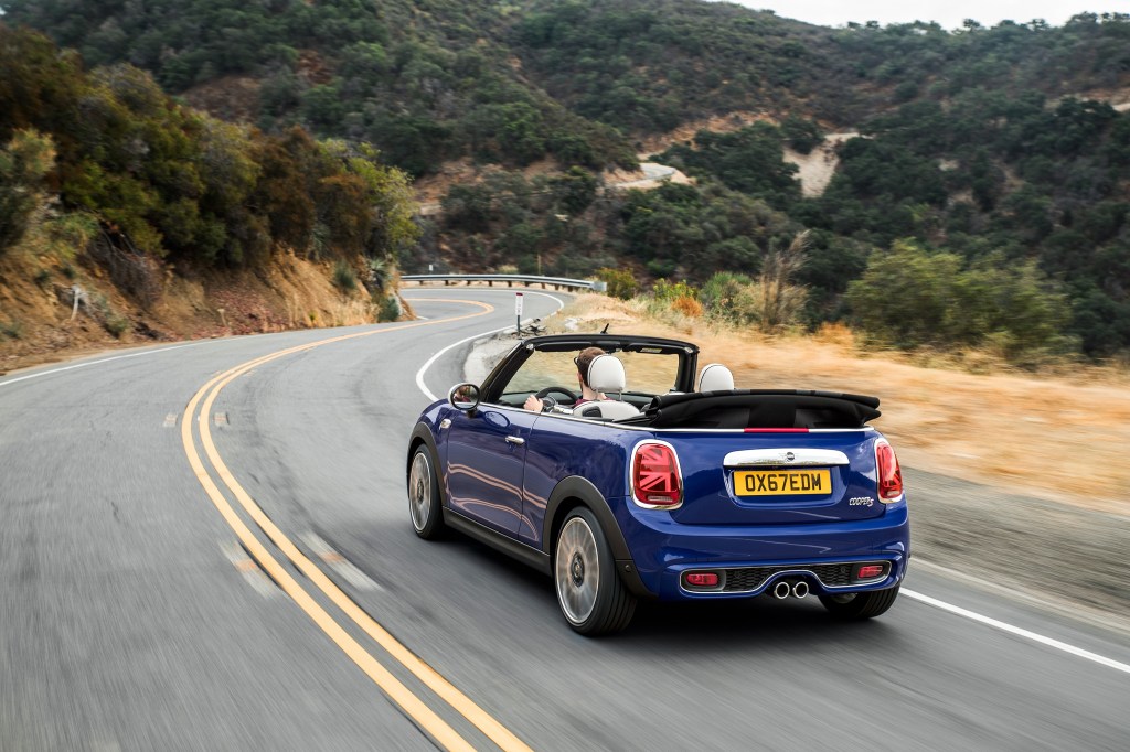The rear 3/4 view of a blue 2022 Mini Cooper S Convertible with its top down driving down a canyon road