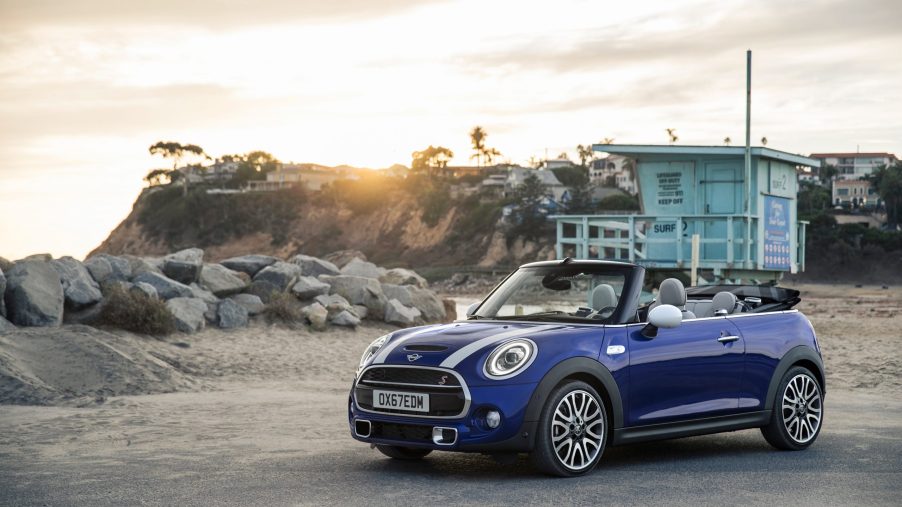 A blue-with-black-stripes 2022 Mini Cooper S Convertible on a beach parking lot at sunset
