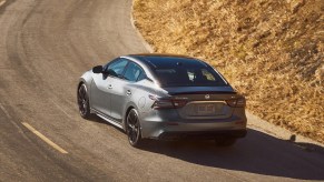 A new 2022 Nissan Maxima in grey driving on a road basked in sunlight