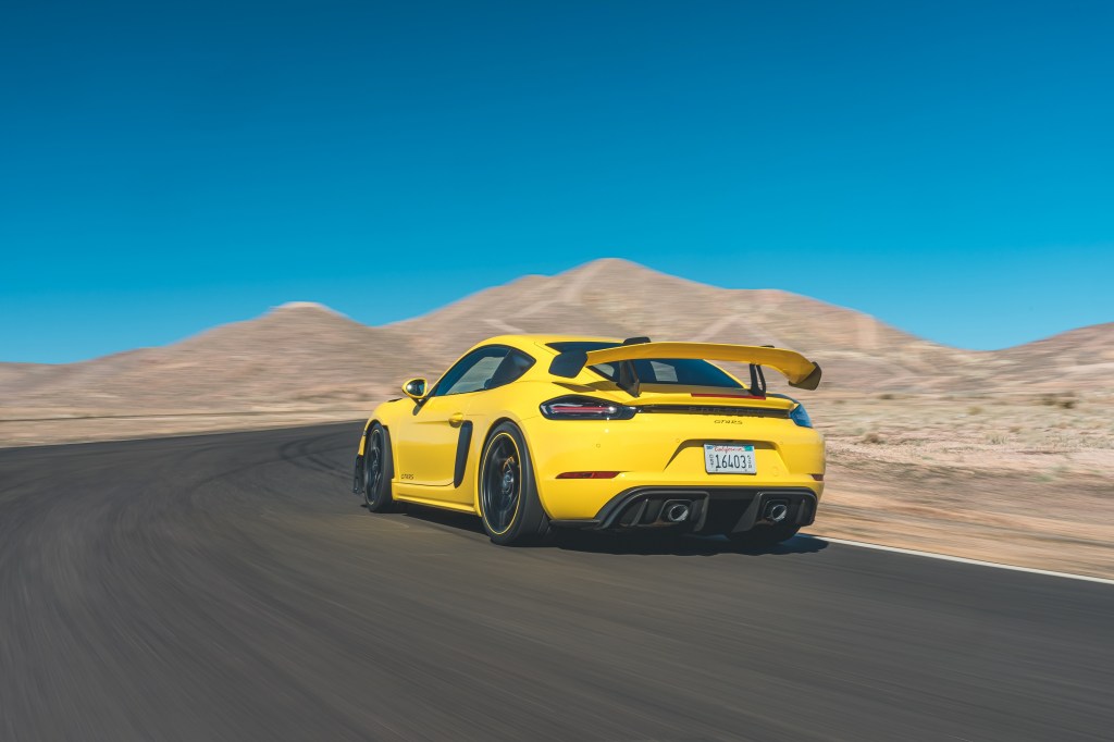 The rear 3/4 view of a yellow 2022 Porsche 718 Cayman GT4 RS going around a desert track corner