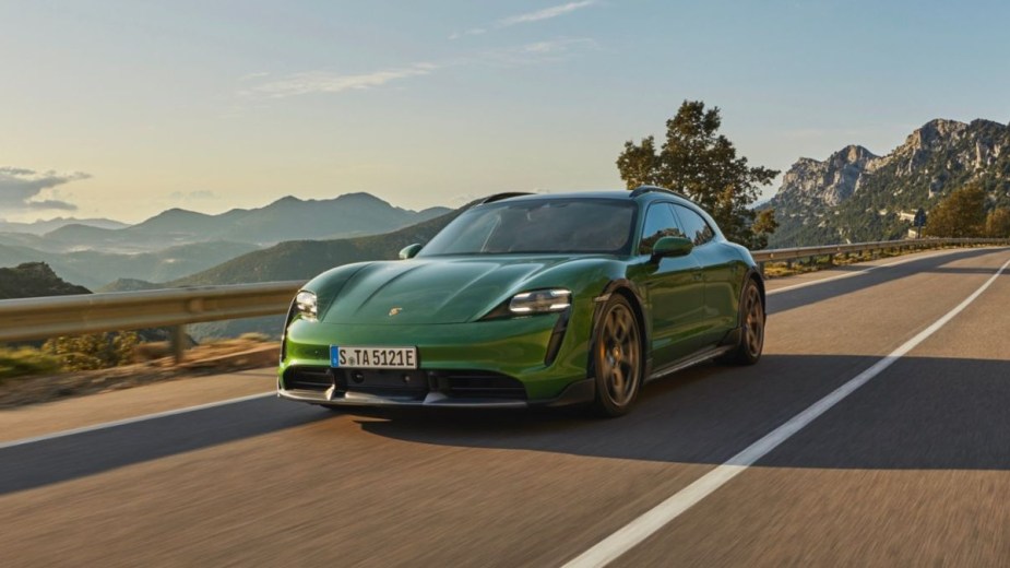 a green 2022 Porsche Taycan Turbo S Cross Turismo is driving along a highway with mountains in the background