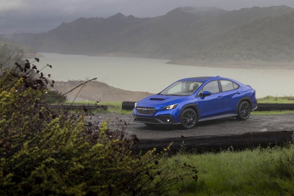 A blue 2022 Subaru WRX parked on a gravel lot next to mountains and a body of water