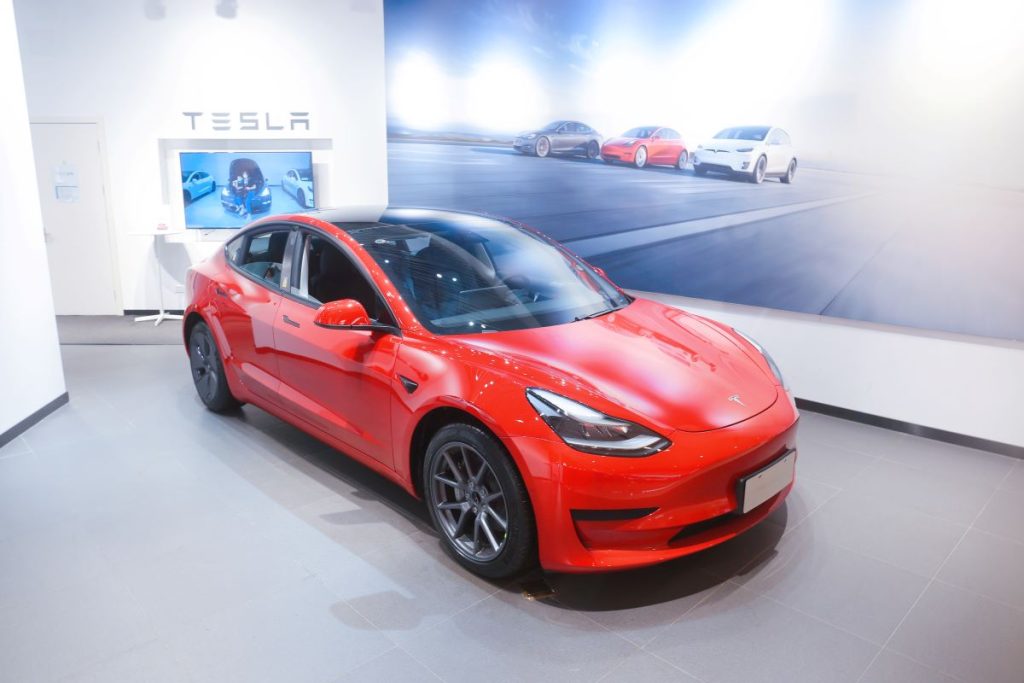 A red 2022 Tesla Model 3 sitting inside a Tesla showroom.