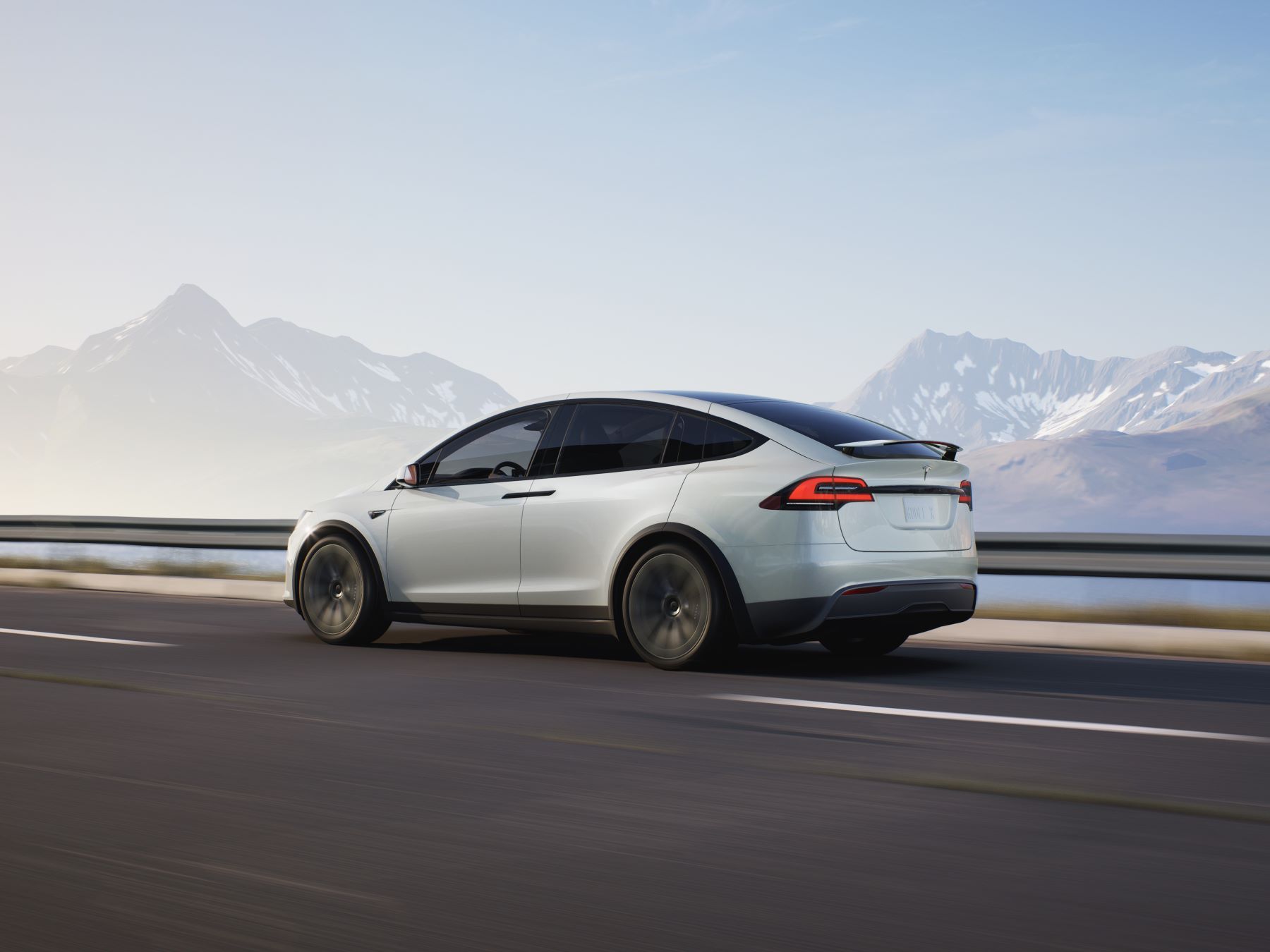 VUS compact tout électrique Tesla Model X 2022 en blanc, prise de vue latérale, roulant sur une autoroute près d'une chaîne de montagnes enneigée