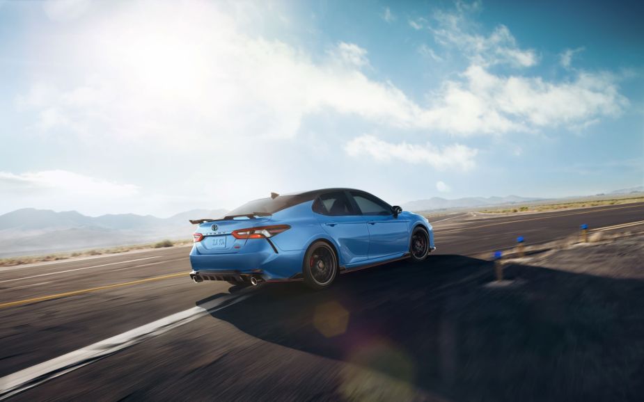2022 Toyota Camry midsize sedan with the TRD performance trim in light blue racing down a highway under a cloudy blue sky