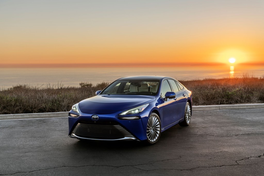 A blue 2022 Toyota Mirai in front of a body of water with a sunset. 