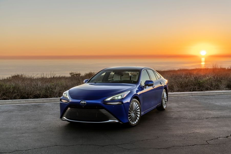 A blue 2022 Toyota Mirai in front of a body of water with a sunset.