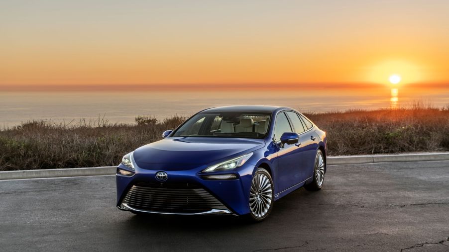 A blue 2022 Toyota Mirai in front of a body of water with a sunset.