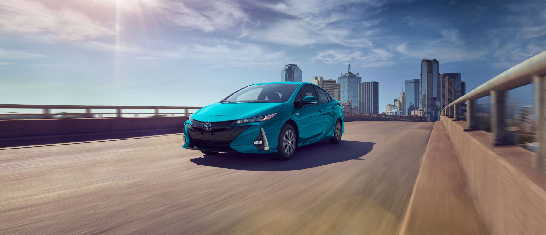 The 2022 Toyota Prius Prime plug-in hybrid (PHEV) hatchback in teal driving over a city bridge