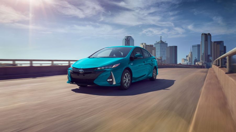 The 2022 Toyota Prius Prime plug-in hybrid (PHEV) hatchback in teal driving over a city bridge
