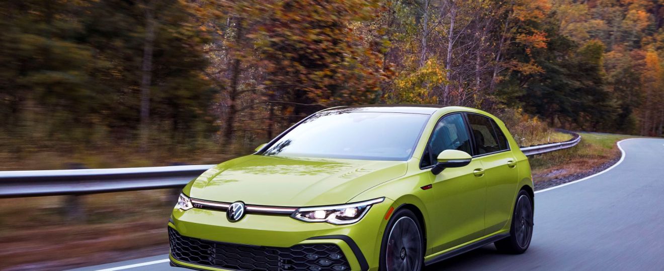 The 2022 Volkswagen Golf GTI performance 'hot' hatchback in yellow driving through a autumn forest highway