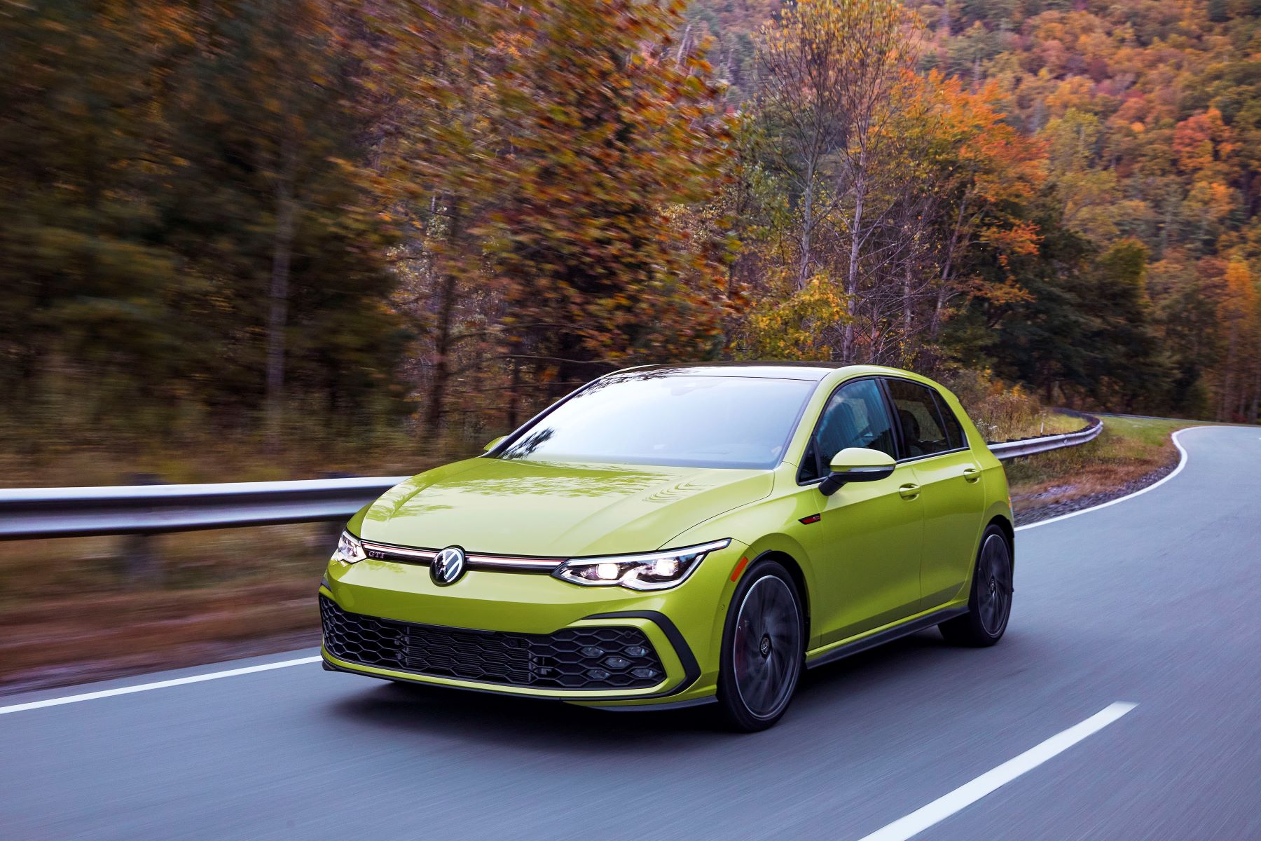 The 2022 Volkswagen Golf GTI performance 'hot' hatchback in yellow driving through a autumn forest highway
