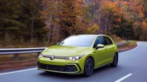 The 2022 Volkswagen Golf GTI performance 'hot' hatchback in yellow driving through a autumn forest highway
