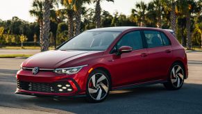 The 2022 Volkswagen Golf GTI sporty hot hatch hatchback in red parked on an asphalt lot surrounded by tropical trees