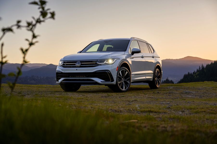 A silver Volkswagen Tiguan sitting in a green area outdoors with mountains in the background.