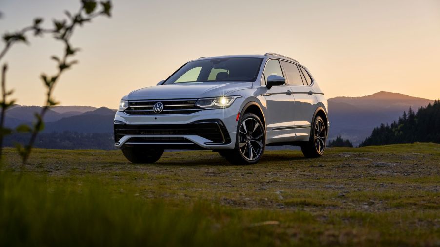 A silver Volkswagen Tiguan sitting in a green area outdoors with mountains in the background.