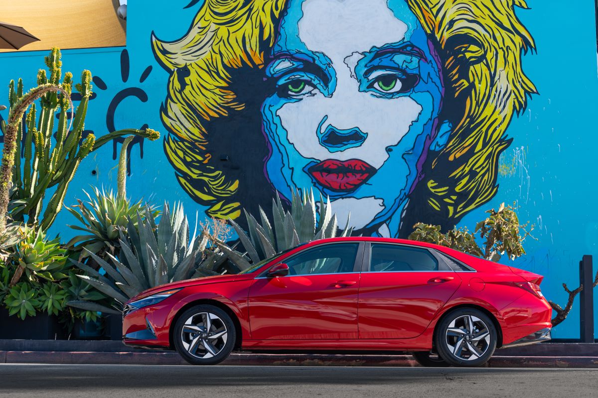 Side view of a red 2022 Hyundai Elantra sedan, one of the best new cars under $20,000, parked in front of a large mural