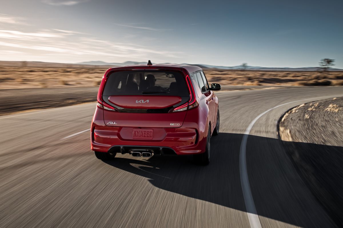 Rear view of a red 2022 Kia Soul, a new car under $20,000, driving along a paved road in the desert