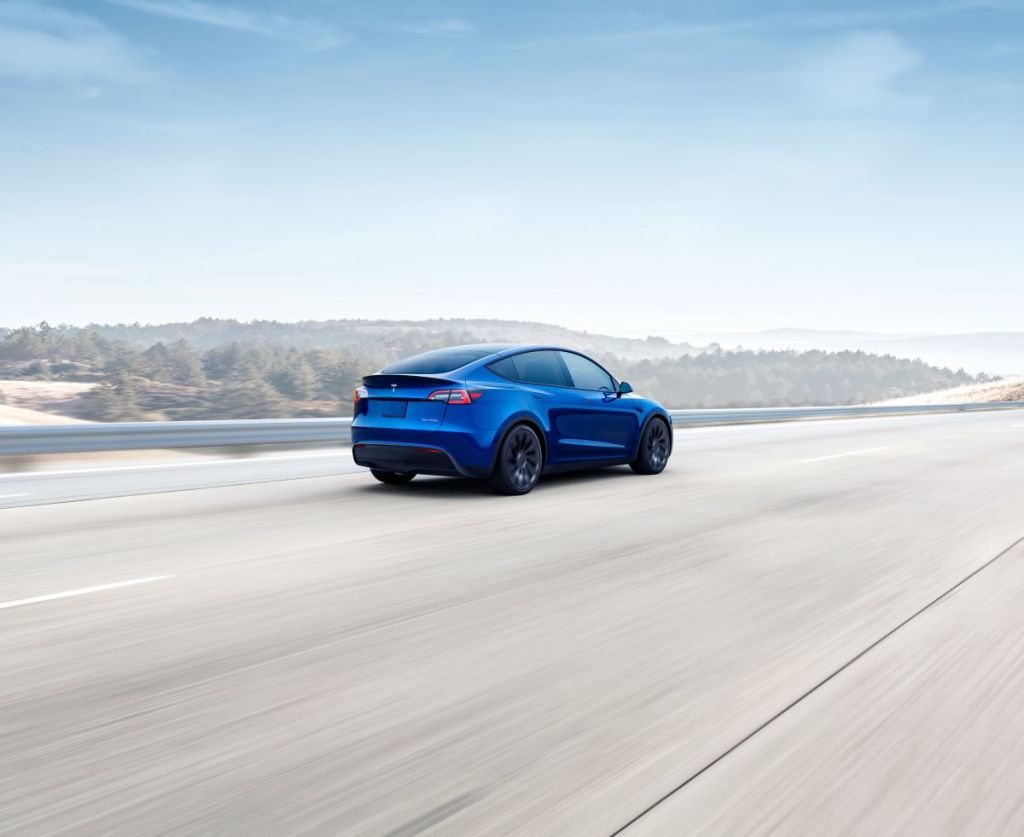 Blue 2022 Tesla Model Y, the best electric SUV, driving fast along a light-colored paved road