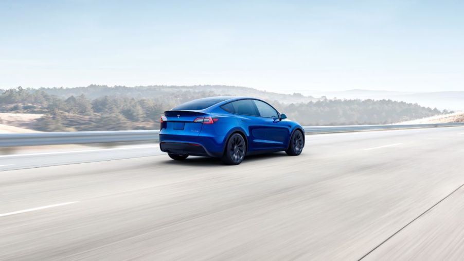 Blue 2022 Tesla Model Y, the best electric SUV, driving fast along a light-colored paved road