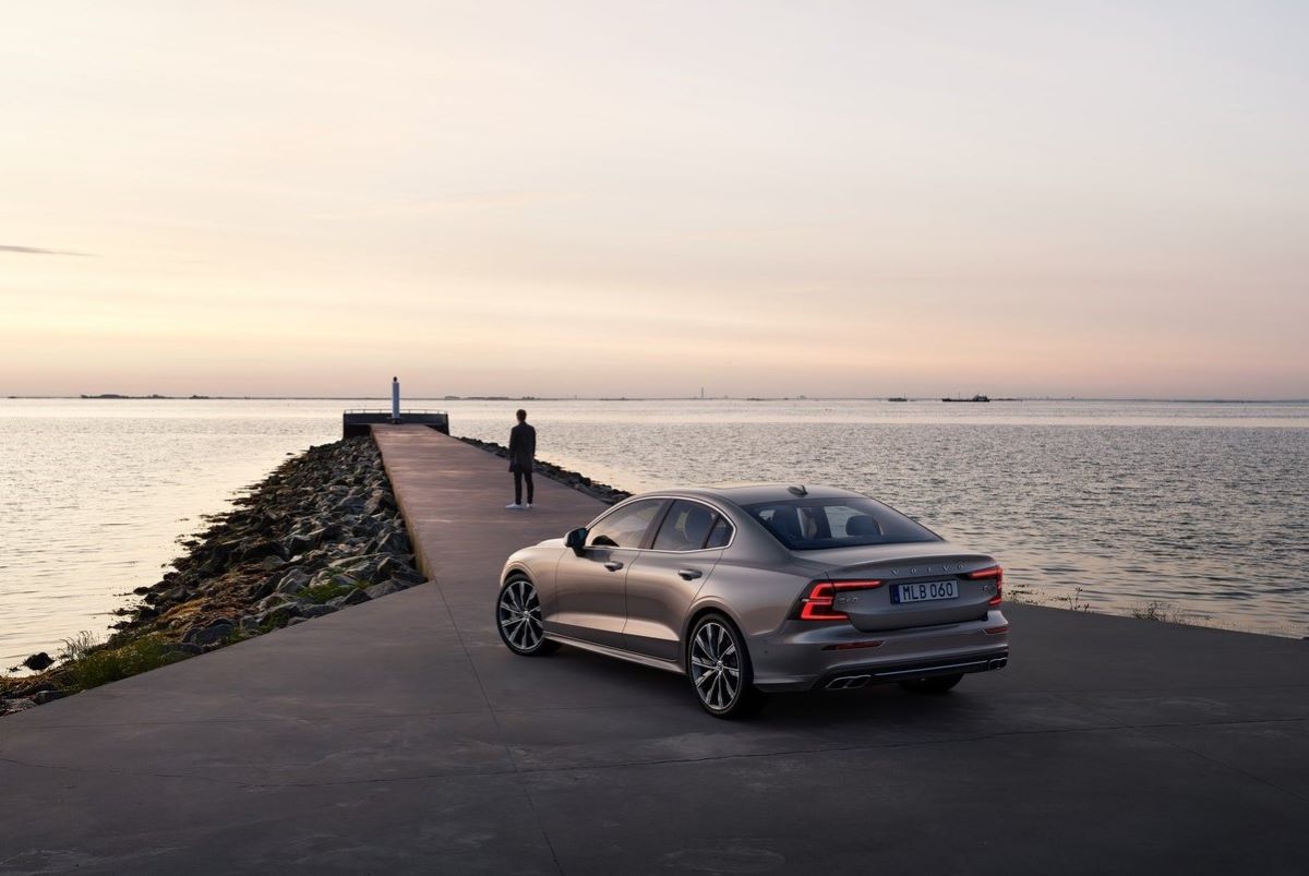 A Volvo S60 sedan, one of the best electric cars, parked on a causeway near the sea, pointing to the horizon as the sun sets