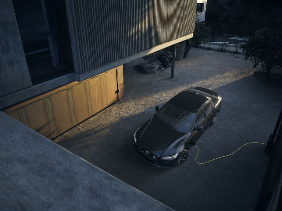 A black Volvo S60 Recharge Plug-In Hybrid sedan parked in a driveway and attached to a charging plug