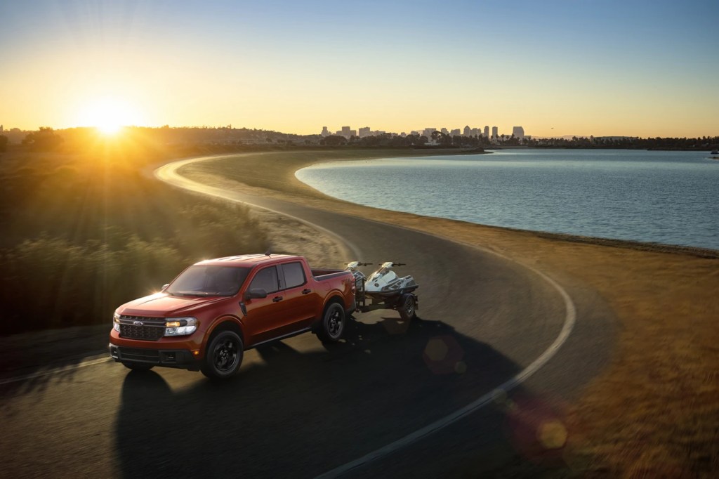 A red 2022 Ford Maverick tows a small boat on a waterfront road. common questions about the compact truck have simple answers.