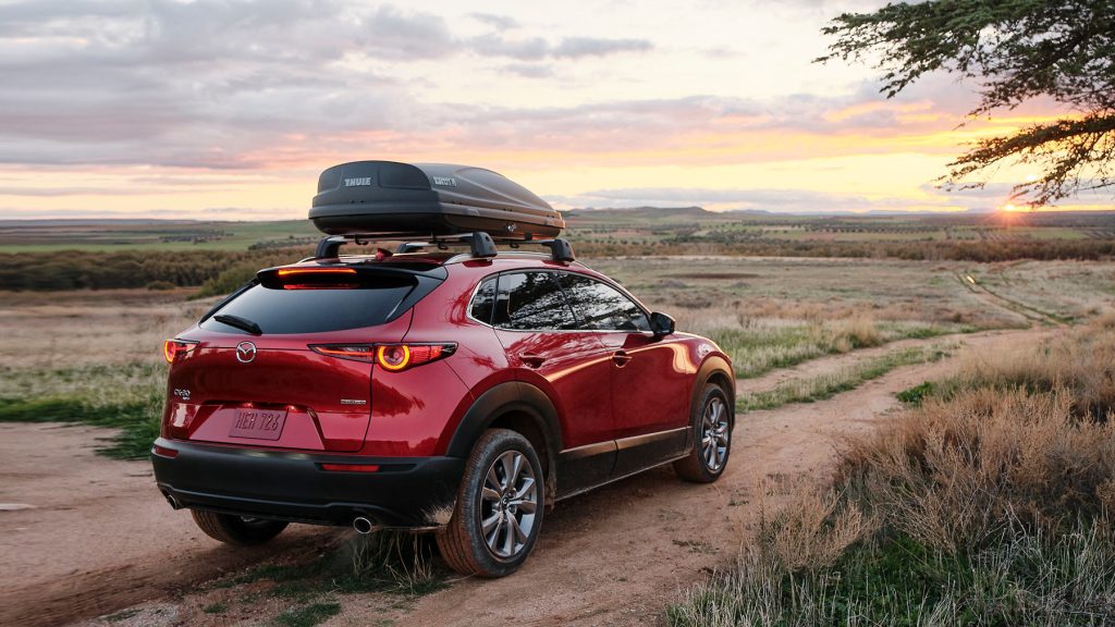 A red 2022 Mazda CX-30 carries a roof rack on top, with a sunset in the background.