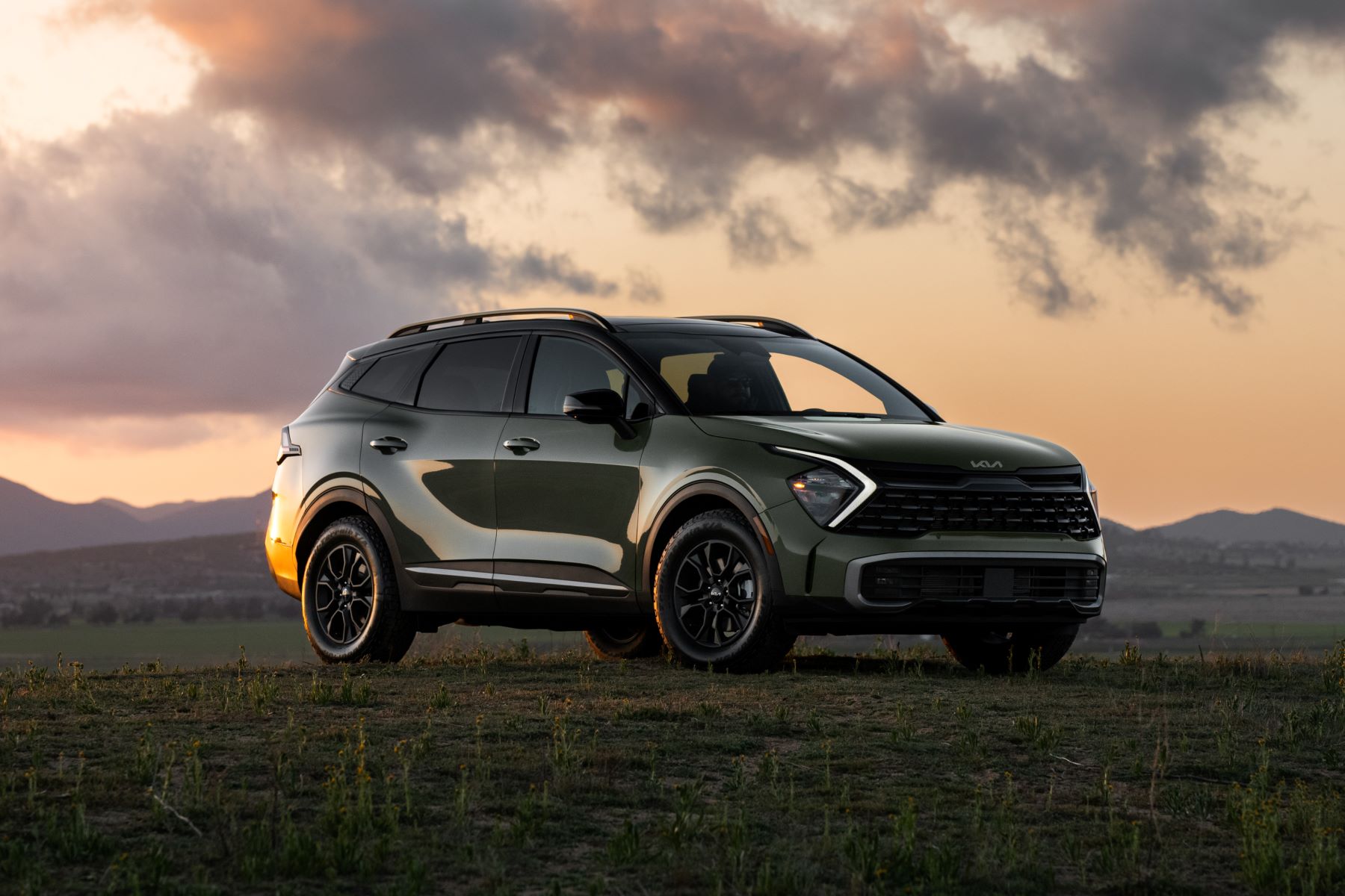 The redesigned 2023 Kia Sportage X-Pro compact SUV parked on an empty field under a orange sunset sky