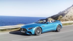 A blue 2023 Mercedes-AMG SL 43 driving down the road with its top down and spoiler up