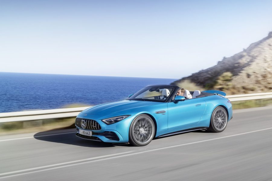 A blue 2023 Mercedes-AMG SL 43 driving down the road with its top down and spoiler up