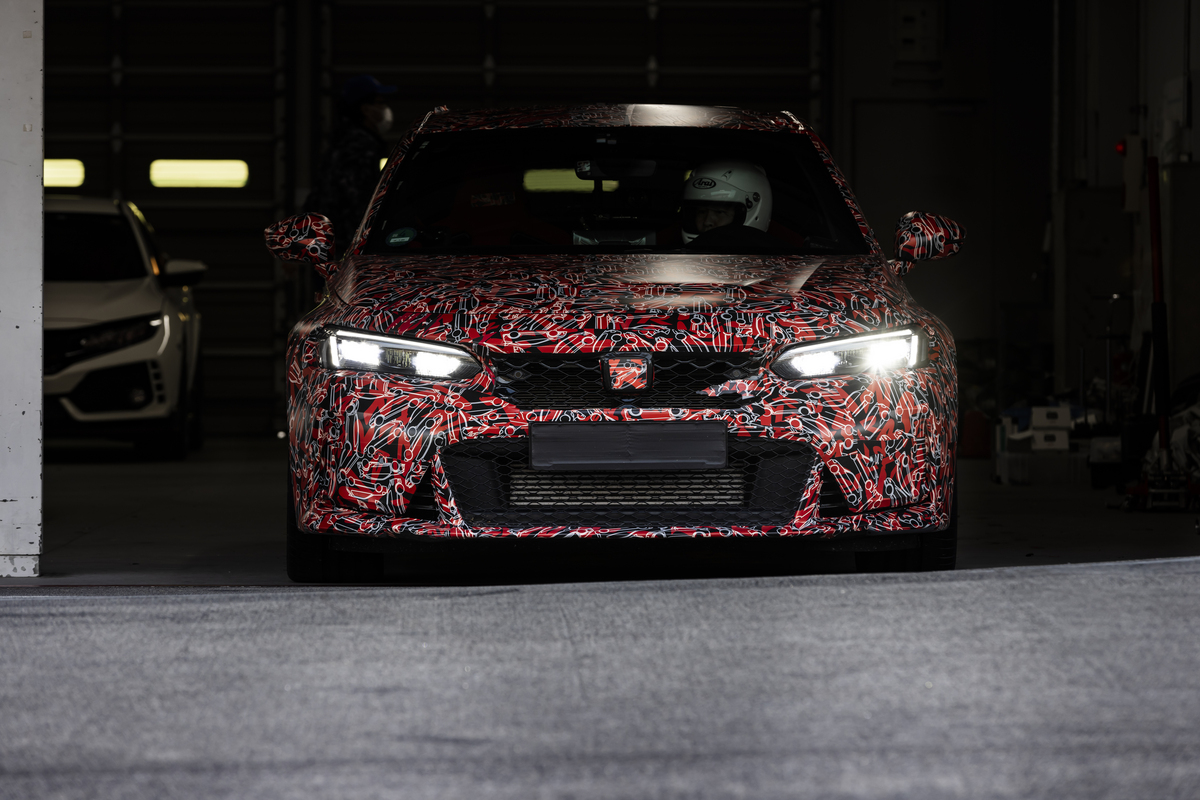 A heavily camouflaged 2023 Honda Civic Type R rolls out from a garage with a racecar driver in the driver's seat