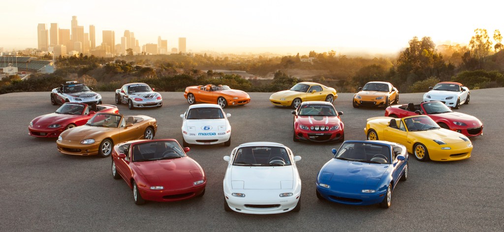 A parking lot full of various MX-5 internal combustion Miatas from the roadster's history.