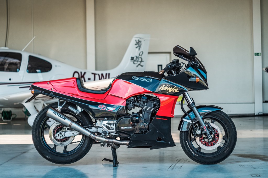 A black-and-red Kawasaki GPZ900R aka Ninja 900 similar to the one in Top Gun in front of an airplane