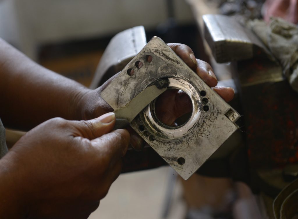 A mechanic cleans part of a disassembled car alternator with a scraper