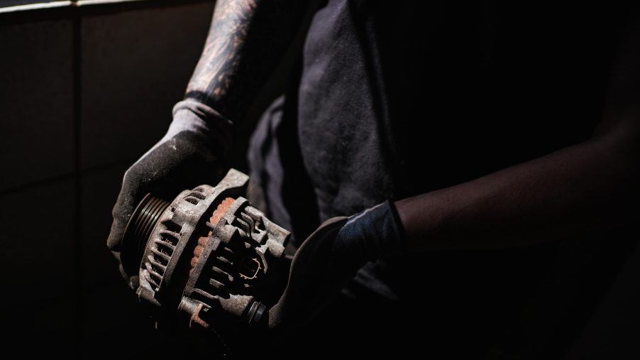 An engineer holds a dismantled old car alternator in a garage