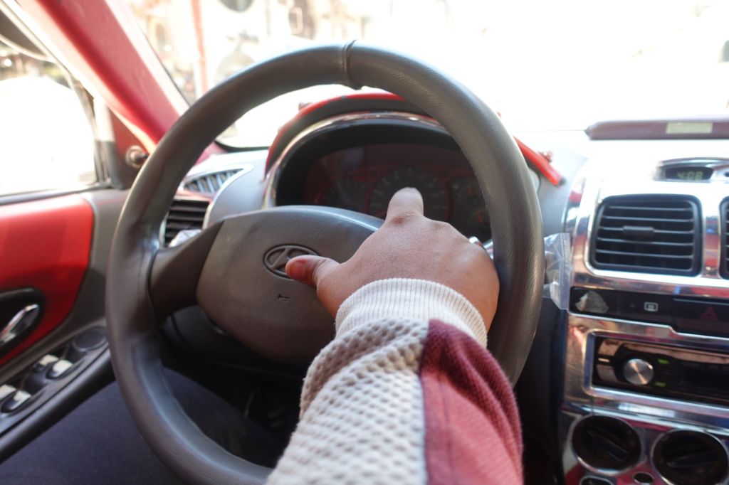 A car horn button on a steering wheel with someone's hand on it. 