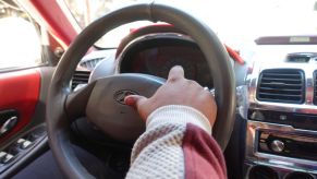 A car horn button on a steering wheel with someone's hand on it.