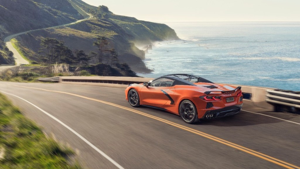 an orange chevrolet corvette c8 drives along a cliffside road showing off its supercar performance and handling