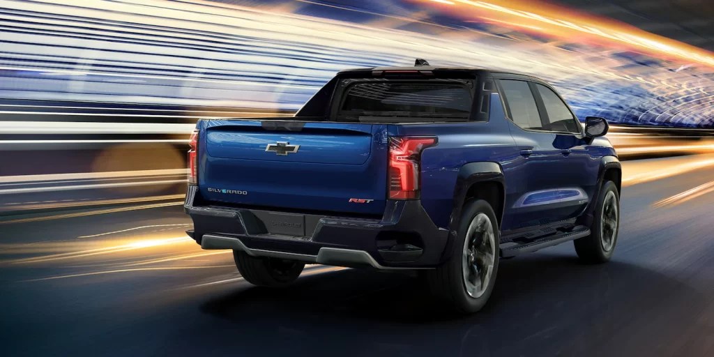 A blue Chevy Silverado EV is featured driving fast as lights are blurred behind it.
