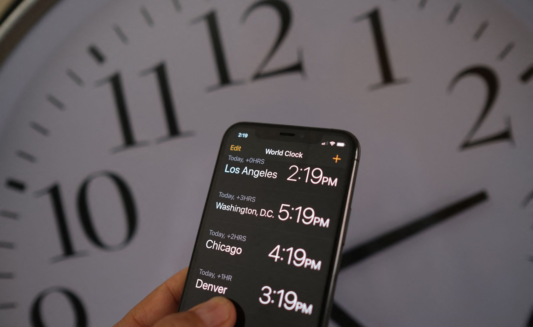 Daylight Savings Time graphic with a smartphone looking at World Clock app times with an analog clock in the background