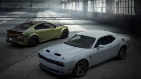 A white Dodge Challenger and green Dodge Charger parked in a warehouse.