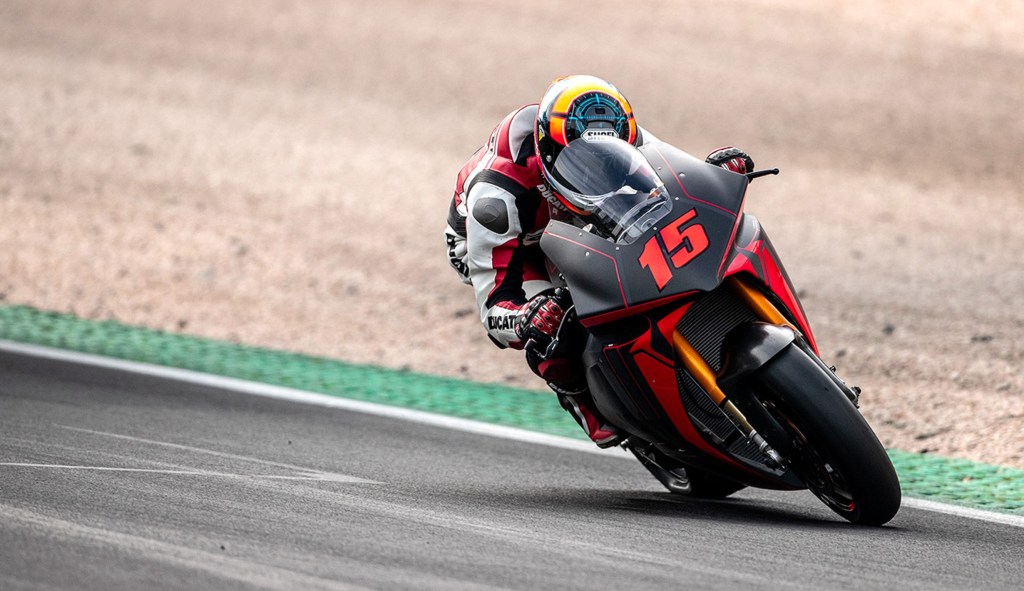 The front view of a Ducati test rider taking a track corner on the red-and-black Ducati V21L MotoE electric motorcycle prototype