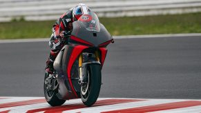 A black-clad rider taking the red-and-black Ducati V21L MotoE electric motorcycle prototype around a track