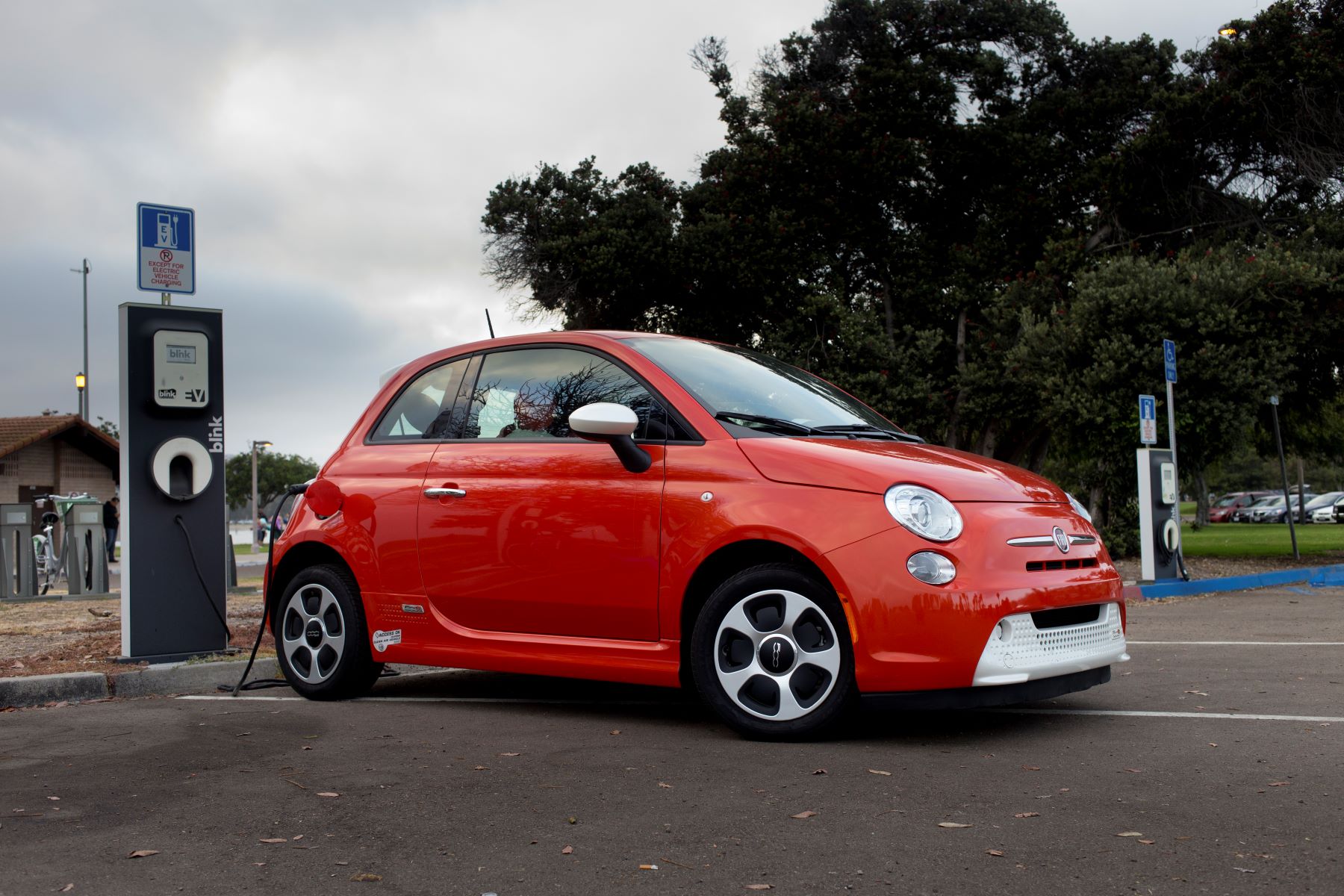 A red Fiat 500e electric vehicle (EV) plugged into a charging station