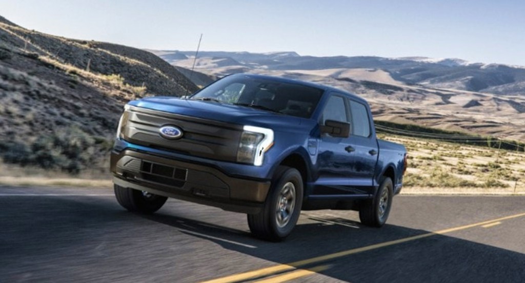 A blue 2022 Ford F-150 Lightning electric pickup truck is driving on the road.  