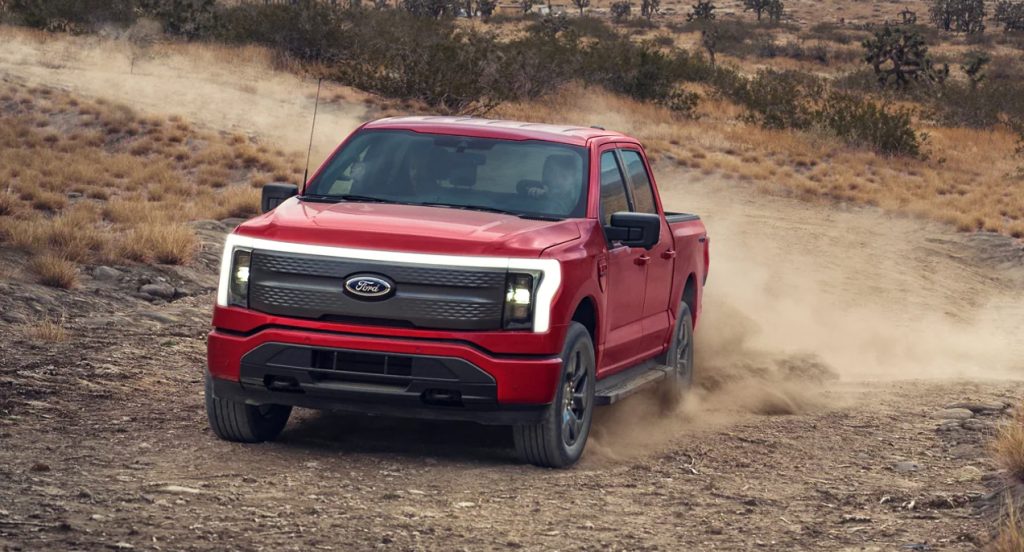 A red 2022 Ford F-150 Lightning electric pickup truck is driving off-road.
