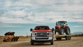 Ford Super Duty pickup truck towing a tractor on a trailer across a farm field.