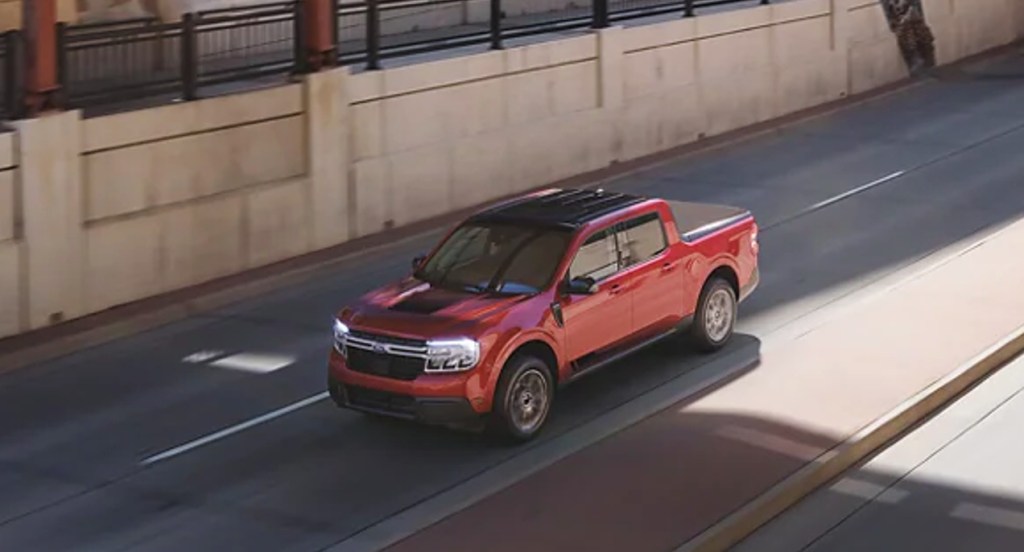 A red 2022 Ford Maverick small pickup truck is driving on the road. 